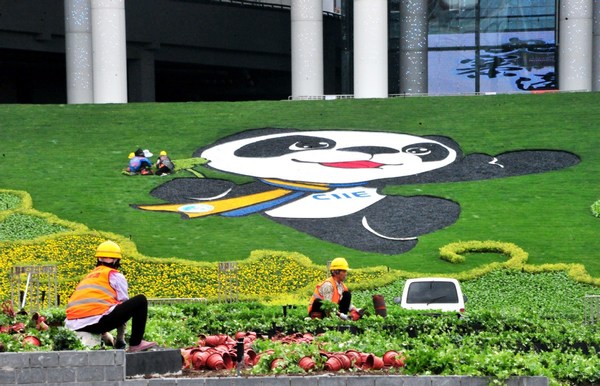 Gardeners trim a lawn featuring the image of Jinbao, the mascot of the China International Import Expo, at the National Exhibition and Convention Center in Shanghai on Oct 15. [Photo by Yang Jianzheng/For China Daily]