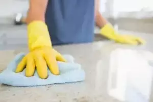 Marble counter being wiped by a blue wiping cloth by a person who's wearing yellow gloves.